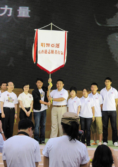 黎明及香港志願者協會副主席林亨利先生從亞組委志願者部宣傳策劃辦公室副主任呂娜(右七)手中接過廣州亞運會志願者旗幟後,高高舉起。右八為廣播處長黃華麒先生。